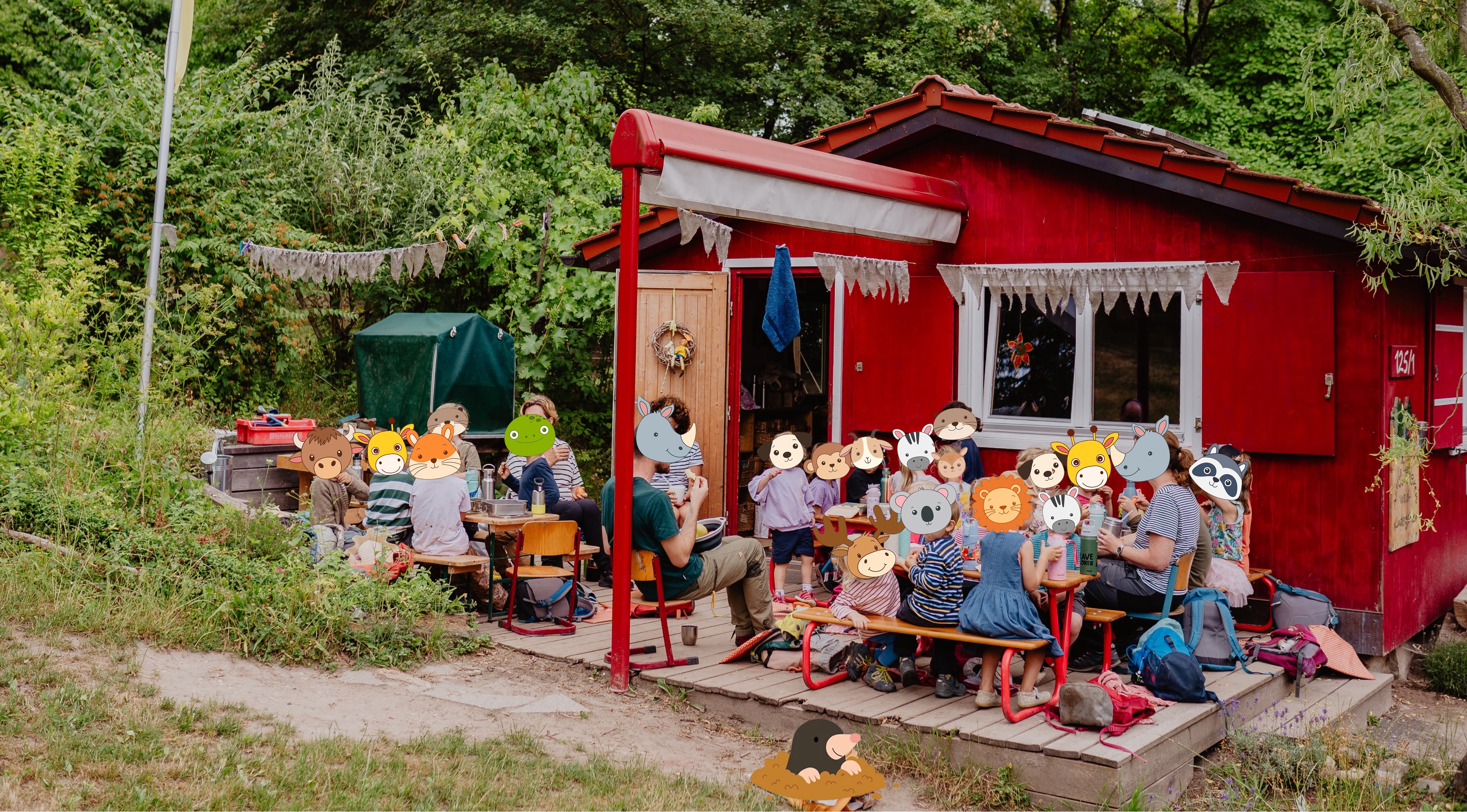 Kinder und Erwachsene vor der roten Hütte des Astrid Lindgren Waldkindergartens